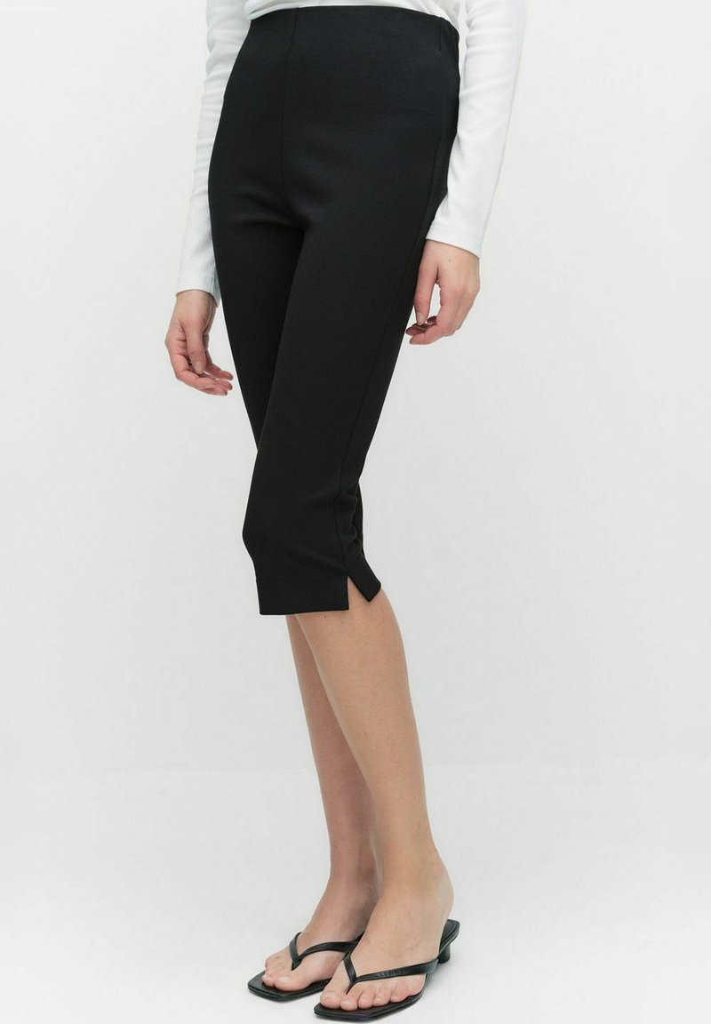 Svarta korta leggings med hög midja, med en mjuk textur och sidofickor vid fållen, som matchas med svarta flip-flops.