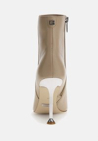 Botín de cuero beige con cremallera trasera, punta afilada y un alto tacón de aguja metálico. Detalle con el logo G en la parte posterior.