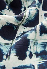 Tissu en coton présentant un motif abstrait bleu marine et bleu clair avec des effets de coups de pinceau. Texture douce, avec des plis et des froissements visibles.