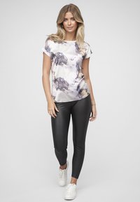 Kortermet, lys lilla topp med abstrakte grå og gull mønstre, kombinert med svarte leggings og hvite joggesko. Glatt, blankt stoff.