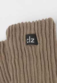 Beige gerippte Strickhandschuhe mit einem schwarzen Etikett, auf dem in weißer Schrift "clz." steht. Der Stoff wirkt weich und dehnbar, entworfen für Komfort und Wärme.