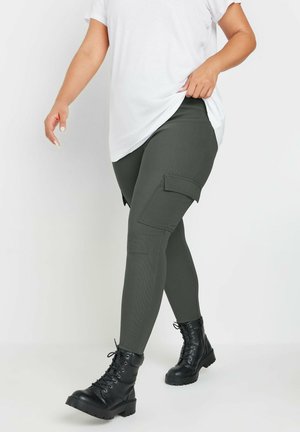 I leggings cargo verdi presentano un tessuto testurizzato, tasche laterali e una vita elasticizzata, abbinati a stivali neri con lacci stile militare.