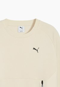 Felpa crema con colletto a costine, caratterizzata da un logo Puma nero e un dettaglio zip laterale. Tessuto morbido e design dal taglio rilassato.