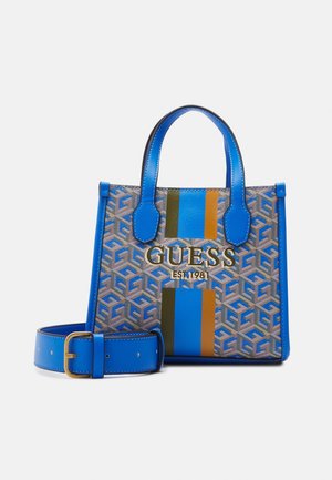 Mała niebieska torba typu tote z wzorem, podwójnymi uchwytami, pionowymi paskami, napisem „GUESS EST 1981” oraz pasujący do niej niebieski pasek z pozłacaną klamrą.