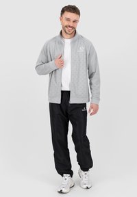 Grå zip-up jakke med en geometrisk mønster, parret med sorte træningsbukser og hvide sneakers. Sættet har et sporty design og en komfortabel pasform.