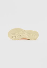 Semelle de chaussure de couleur crème avec des rainures texturées et un motif swoosh sur un fond gris clair uni.