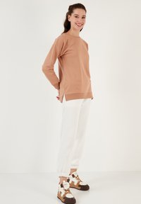Maglietta chiara a maniche lunghe con spacchi laterali, abbinata a pantaloni jogger con polsini elastici bianchi e sneakers alte multicolori e texture.