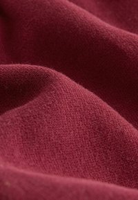 Bordeaux stof med en blød, tekstureret overflade. Materialet fremstår en smule fluffy med synlige fibre og bløde folder.