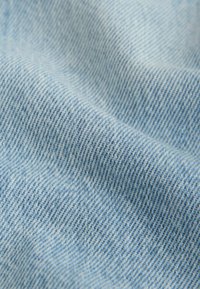 Gros plan sur un tissu denim bleu clair avec une texture de tissage diagonale visible et des plis doux.