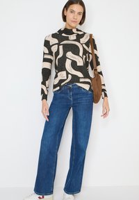 Top de manga larga con estampado en negro y crema, combinado con jeans azules de pierna ancha y zapatillas blancas, complementado con un bolso marrón de hombro.