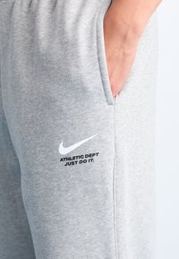 Pantalons de survêtement gris en tissu doux avec une poche latérale. Présente un logo Nike swoosh blanc et l'inscription "ATHLETIC DEPT JUST DO IT".