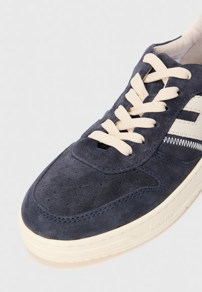 Dark blue suede sneaker with cream laces and sole, featuring perforated toe area and stitched side design on a white background.