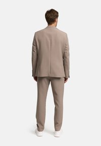 Beige pak gemaakt van getextureerde stof, met een getailleerd colbert en recht gesneden broek, gecombineerd met witte sneakers.