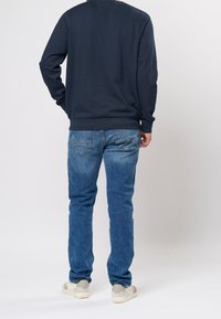 Sweat-shirt bleu marine à manches longues, col rond ; associé à un jean denim bleu. Le jean comprend des poches arrière et un effet délavé ; chaussures décontractées visibles.