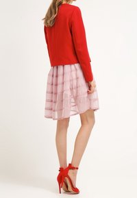Czerwona dopasowana kurtka z długimi rękawami w połączeniu z jasnoróżową warstwową sukienką. Czerwone szpilki uzupełniają całość.
