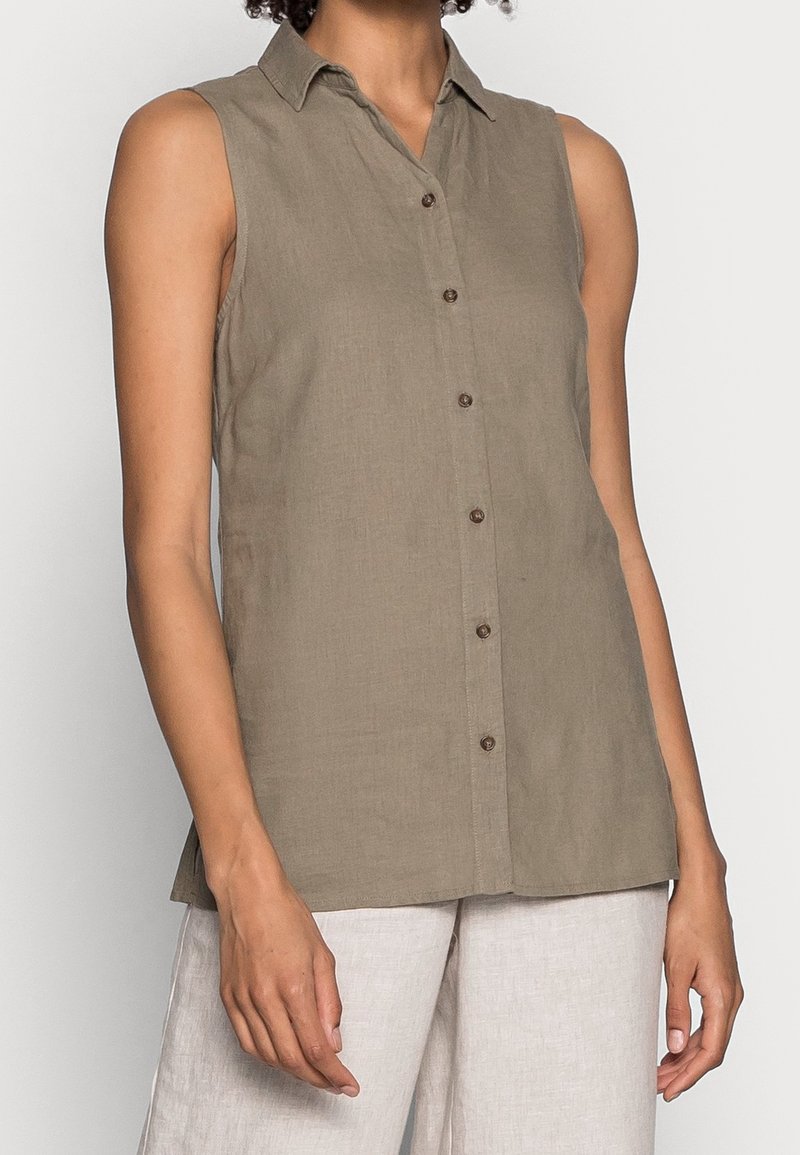 Camicia senza maniche color nocciola con colletto a punta e pattina frontale. Realizzata in lino con una superficie leggermente texture.
