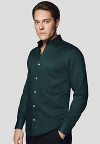 Ciemnozielona koszula z długim rękawem, o strukturalnym kołnierzyku, z guzikami i gładką teksturą. Charakteryzuje się dopasowanym krojem oraz klasycznym zapięciem na guziki.