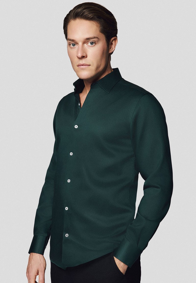 Ciemnozielona koszula z długim rękawem, o strukturalnym kołnierzyku, z guzikami i gładką teksturą. Charakteryzuje się dopasowanym krojem oraz klasycznym zapięciem na guziki.
