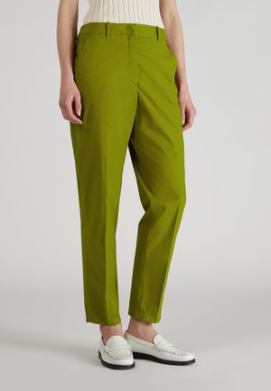 Pantalons droits légers et verts, avec une texture lisse, dotés de poches avant et d'une coupe ajustée. Associés à des mocassins blancs.