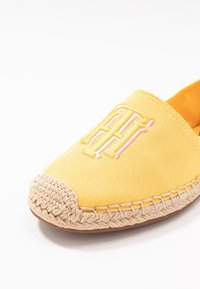Espadrille en toile jaune avec semelle en jute tressé, ornée d'initiales brodées dans un design rose et blanc sur la partie supérieure.