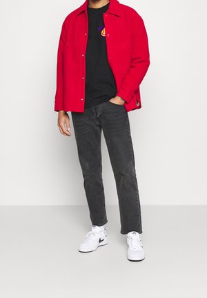 Rode katoenen shirtjacket, zwart T-shirt met een grafisch ontwerp, donkere jeans en witte sneakers. Het jack heeft twee voorkantenzakken en drukknoopsluitingen.