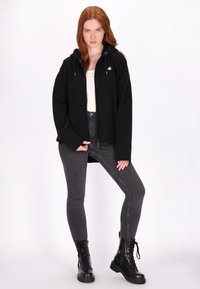 Zwarte rits-huistrui met trekkoorden en een klein logo, gecombineerd met grijze skinny jeans en zwarte veterschoenen.