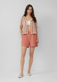 Gestreept gebreid T-shirt met korte mouwen in roze en crème, gecombineerd met koraalkleurige hooggetailleerde shorts. Model draagt beige flats.