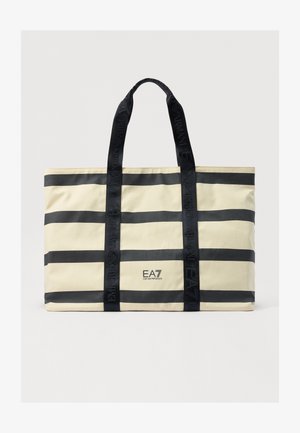 Sac fourre-tout beige avec des rayures horizontales noires, doté de poignées et d'un logo de marque noirs. Fabriqué en tissu durable, de forme rectangulaire.