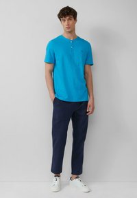 Türkisfarbendes Kurzarm-Henley-T-Shirt mit Knopfdetails, kombiniert mit navyblauen Chinohosen und weißen Sneakers. Minimalistisches Design und Passform.