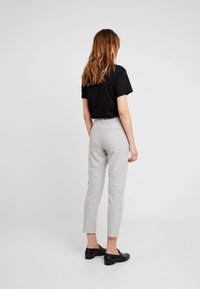 Pantalon à carreaux gris avec une coupe slim et longueur cheville, associé à un t-shirt noir à manches courtes et des mocassins noirs.