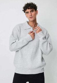 Pull gris texturé avec col et fermeture à demi-glissière. Coupe ample, poignets et ourlet côtelés. Design décontracté avec un motif tissé.