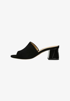 Zwarte suede open-teen mule met een geometrische zwarte blokhak en een gladde beige inlegzool. Strak, minimalistisch ontwerp met een zachte textuur.