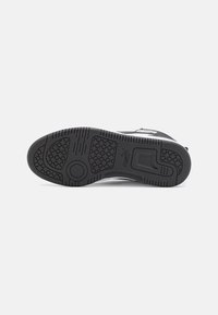 Semelle de basket noire avec motifs de grip texturés, formes circulaires et hexagonales, et logo Puma au centre sur un fond blanc uni.