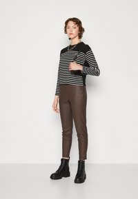Haut à rayures noires et blanches à manches longues, pantalon ajusté marron et bottines noires à lacets. La tenue présente un design minimaliste avec une silhouette courte.