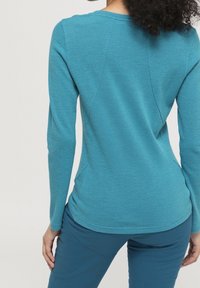Long-sleeve top made of textured blue fabric, featuring a round neckline and fitted silhouette with subtle seam detailing on the back.