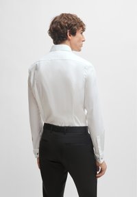 White long-sleeve shirt with a pointed collar, smooth texture, and black cuff links, paired with black tailored trousers.