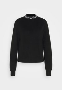 Czarny sweter typu pulower o prążkowanej fakturze, z wysokim kołnierzem i białym paskiem z logo wokół szyi. Długie, dopasowane rękawy.