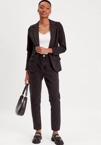 Blazer nero con rever, canotta bianca in pizzo, jeans neri a vita alta e mocassini neri robusti con dettagli in catena argentata. Borsa nera.