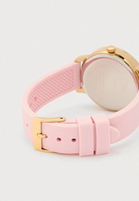 Roze siliconen horlogeband met gouden gesp en ronde horlogekast met gouden rand op een witte ondergrond.