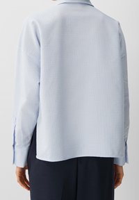 Ljusblå, texturerad skjorta med rutmönster, ryggsöm och långa ärmar med knappmanschetter. Skräddarsydd passform med rundad nederkant.