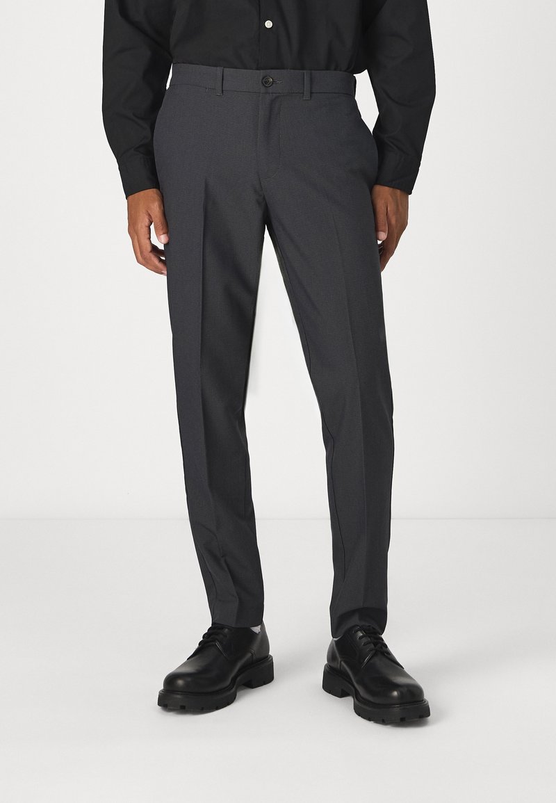 Homme portant un pantalon de costume slim gris foncé avec des chaussures en cuir noir à lacets et une chemise noire à boutons.
