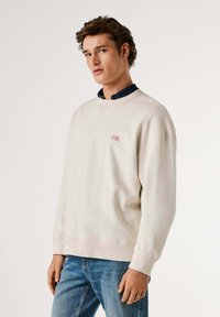 Felpa maglione color beige chiaro in misto cotone, con scollo a V e logo "PJL" ricamato in rosso sul petto. Vestibilità casual, polsini a costine.