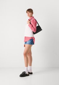 Svart håndveske med minimal maskinvare, rød og hvit stripete langermet skjorte, hvit tanktop, denimshorts og svarte sko med stropper.