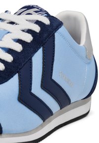 Baskets bleu clair avec empiècements en daim bleu marine, lacets blancs, col rembourré blanc et « STADION » imprimé sur le côté en beige.