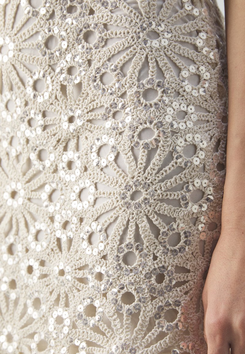 Beige gehäkelter Stoff, der mit runden Pailletten geschmückt ist und komplizierte Blumenmuster sowie Durchbrüche im gesamten Design aufweist.