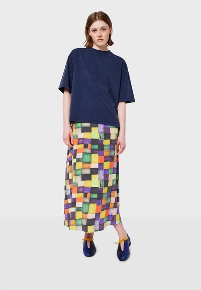 T-shirt oversize blu navy abbinato a una gonna maxi colorata e stampata con quadrati verdi, gialli, viola e arancioni. Scarpe blu scuro in evidenza.