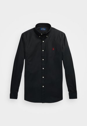 Sort skjorte med knapper og en skarp krave, med hvide knapper og et lille rødt broderet logo på venstre bryst. Lavet af bomuldsstof.
