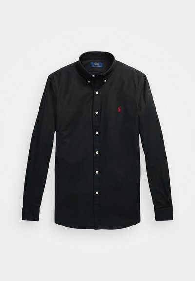 Camisa preta de botão com colarinho bem definido, apresentando botões brancos e um pequeno logótipo bordado em vermelho no lado esquerdo do peito. Material de algodão.