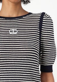 Top a righe in maglia blu navy e crema, con maniche a palloncino corte e scollatura rotonda. Piccolo logo ricamato sul davanti.
