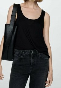 Top sin mangas negro hecho de tela suave, combinado con jeans de mezclilla oscuros de cintura alta. Un bolso tote de cuero negro está colgado de un hombro.